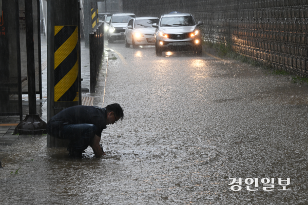 호우주의보가 발효 중인 16일 오후 화성시 병점동 송화초등학교 앞 버스정류장에서 한 시민이 폭우로 도로에 물이 차오르자 손으로 배수구를 뚫고 있다. 2025.9.16 /임열수기자 pplys@kyeongin.com