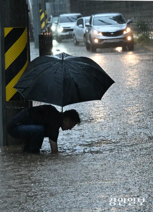 호우주의보가 발효 중인 16일 오후 화성시 병점동 송화초등학교 앞 버스정류장에서 한 시민이 폭우로 도로에 물이 차오르자 손으로 배수구를 뚫고 있다. 2025.9.16 /임열수기자 pplys@kyeongin.com