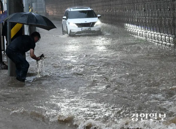 호우주의보가 발효 중인 16일 오후 화성시 병점동 송화초등학교 앞 버스정류장에서 한 시민이 폭우로 도로에 물이 차오르자 손으로 배수구를 뚫고 있다. 2025.9.16 /임열수기자 pplys@kyeongin.com