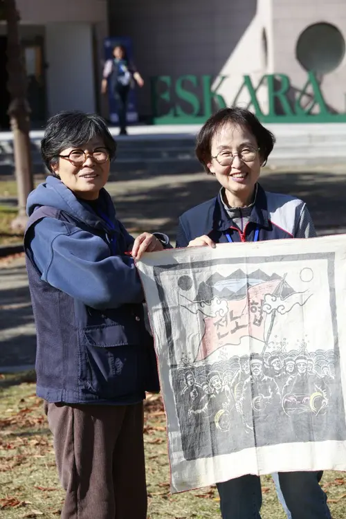 1990년 1월22일, 수원 성균관대학교에서 열린 전국노동조합협의회(전노협) 창립대회 당시 제작했던 천 포스터를 들고 창립식 현장에 있었던 이선희(왼쪽) 민주노총 경기도본부 총무국장과 조귀제 민주노총 경기도본부 부본부장이 행사가 열렸던 건물 앞에서 기념 촬영을 하고 있다. /민주노총 경기도본부 제공