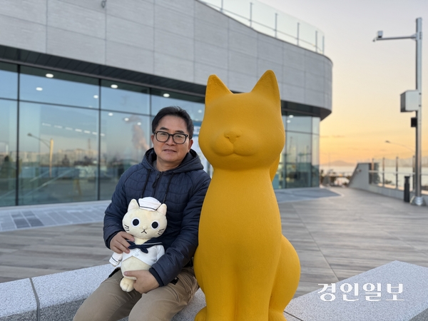 지난 2일 해질 무렵 인천 동구 만석·화수 해안산책로 ‘크로캣 하우스’ 3층에서 만난 허승량 공공스토리사업단 대표. 허 대표 오른쪽에 있는 조형물이 ‘크로캣’, 그가 안고 있는 인형이 크로캣 캐릭터 인형이다. 2026.1.2 /박경호기자 pkhh@kyeongin.com