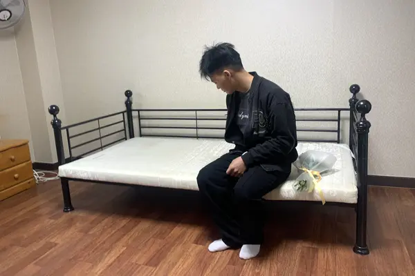 지난 4월10일 뚜안(23)씨의 동생 뚜(21)씨가 형이 생전 머물던 이천의 한 자갈공장 숙소동 기숙사에서 상념에 잠겨 있다. 침대 위에는 형을 추모하기 위해 들고 온 국화꽃이 놓여 있다. 2026.4.10 /유혜연기자 pi@kyeongin.com