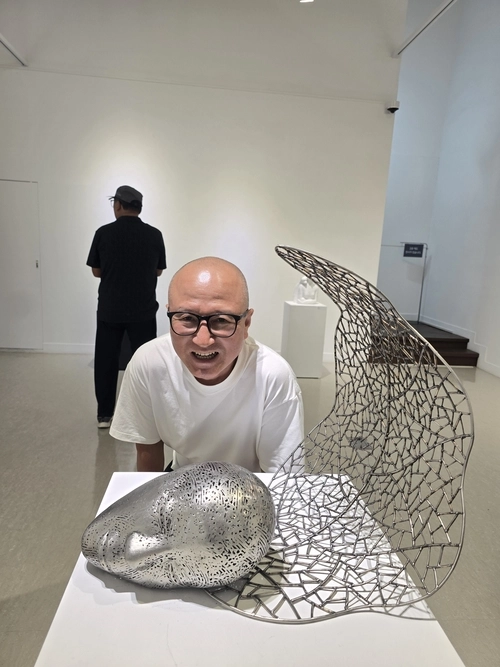 제16회 개인전을 앞둔 강신영 작가가 출품작 ‘숨’(48×48×48㎝, 스테인리스스틸, 2026년작)옆에서 포즈를 취하고 있다.  /강신영조형연구소 제공