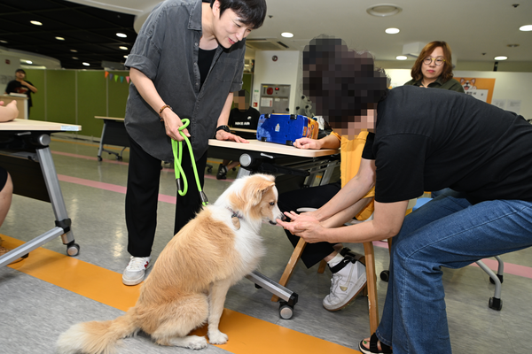 거동이 불편한 참가자에게 천유진 강사가 리겔을 데리고 다가갔다. 참가자가 활동보조사의 도움으로 리겔에게 손을 내밀고 있다. 2026.8.26 /구리시 제공
